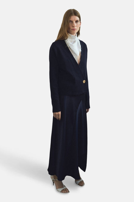 Blauwe MANGO-gilet met gouden knoop, gedragen over een wit overhemd en een marineblauwe lange rok.