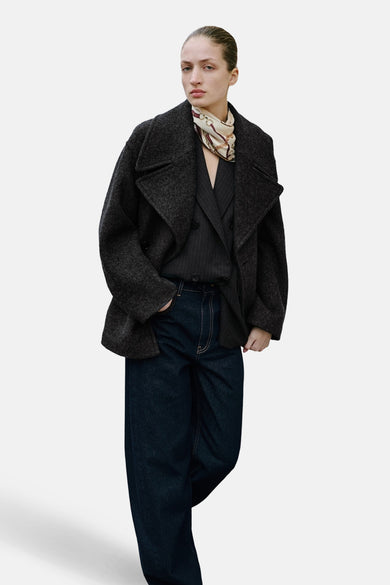 Jean en denim bleu foncé de MANGO, porté avec un veston et un foulard à motifs.
