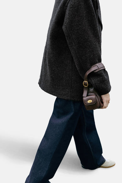 Jean en denim bleu foncé de MANGO, porté avec un manteau gris et un sac à main en cuir marron, en vue latérale.
