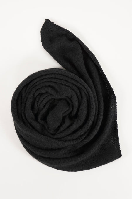 Écharpe noire de PIECES®, tricotée avec une texture douce, enroulée sur un fond blanc.
