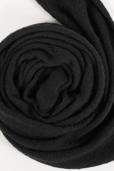 Écharpe noire enroulée de PIECES®, texture tricotée douce visible.