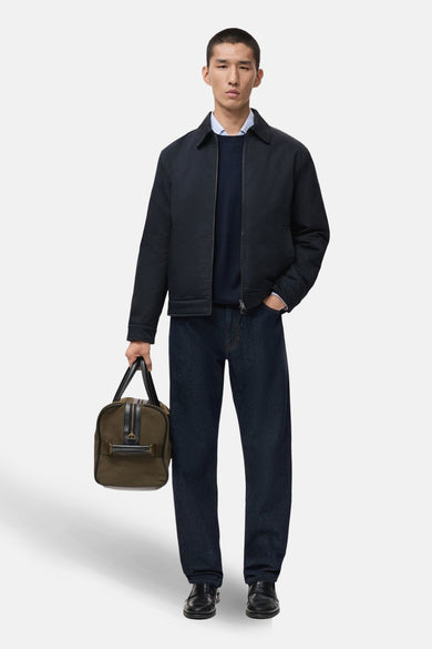 Kort blauw jasje van MANGO, gedragen met een marineblauwe trui, donkere jeans en een groene reistas.