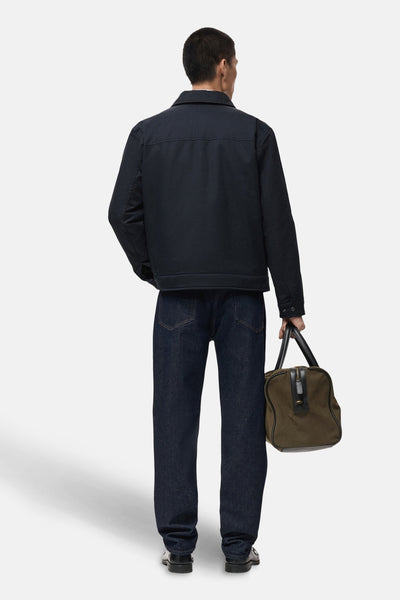 Kort blauw jasje van MANGO, van achteren gezien, gedragen met een donkere jeans en een kaki reistas.