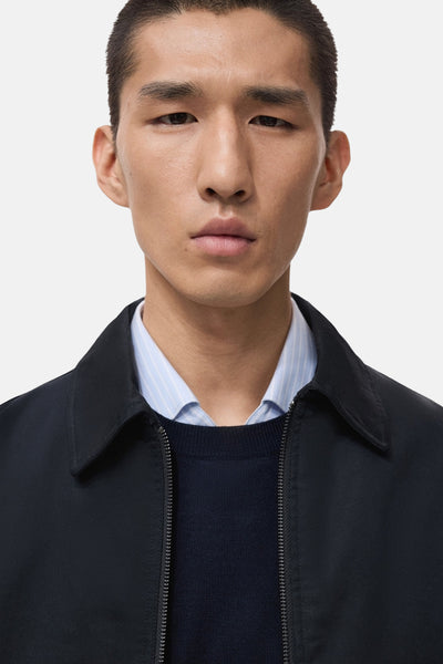 Veste courte bleue de MANGO, portée sur une chemise rayée bleu clair et un pull bleu marine.