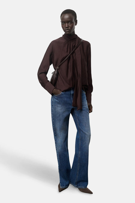 Blouse à manches longues marron par MANGO avec col montant et porté avec un jean bleu.
