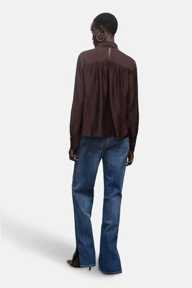 Chemisier à manches longues marron, de MANGO, avec un détail de découpe au dos, porté avec un jean bleu.