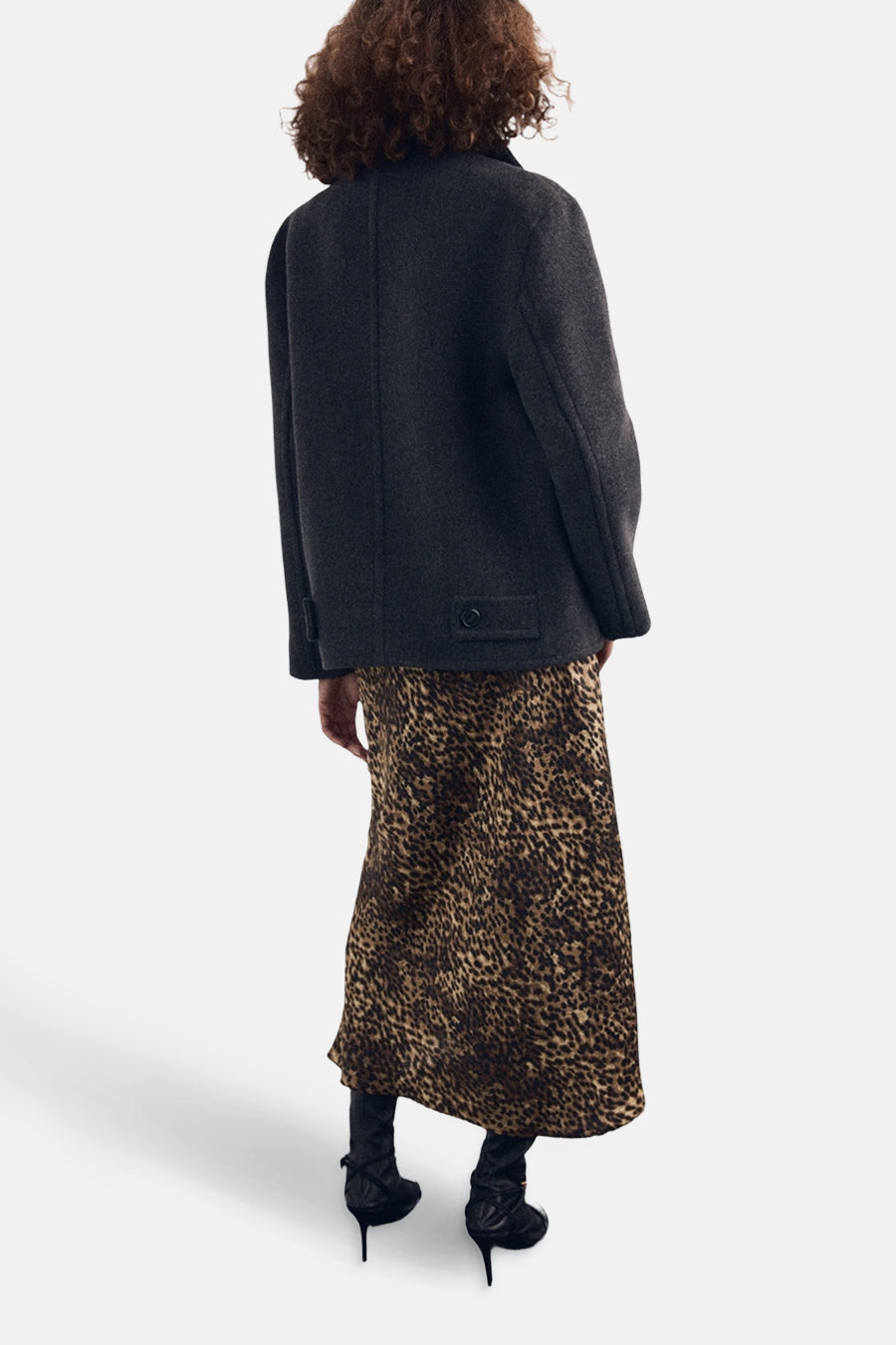 Jupe mi-longue imprimée multicolore de MANGO, portée avec un manteau gris et des bottines noires à talons hauts.