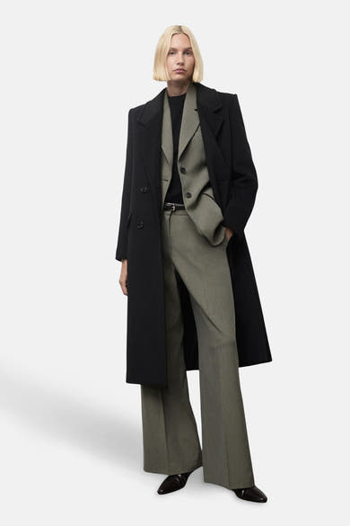 Pantalon vert MANGO, porté avec une ceinture noire, un blazer et un manteau longs noirs.