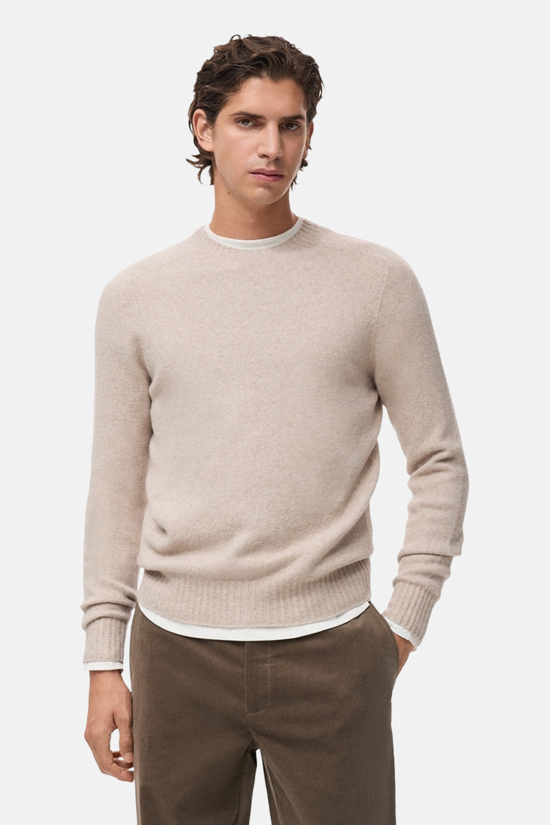 Pull à col rond beige de MANGO, porté avec un t-shirt blanc et un pantalon en velours côtelé marron.