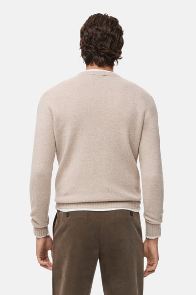 Pull à col rond beige de MANGO, porté avec un pantalon marron et un t-shirt blanc, vue de dos.