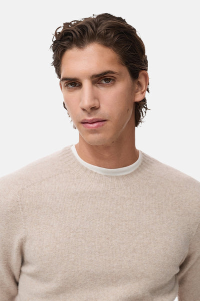 Pull à col rond beige de MANGO, avec une texture en tricot fin et un sous-vêtement blanc visible.