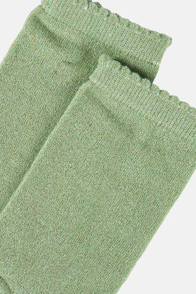 Chaussettes vertes de PIECES®, en maille brillante avec bordure ondulée, présentées en angle.
