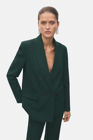 Groene blazer van MANGO, dubbelgeknoopt, gedragen met een bijpassende broek en lange oorbellen.