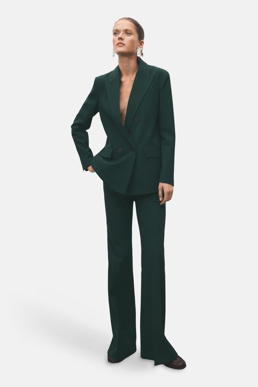 Blazer vert par MANGO, coupe croisée à double boutonnage, porté avec un pantalon assorti et des boucles d'oreilles pendantes.