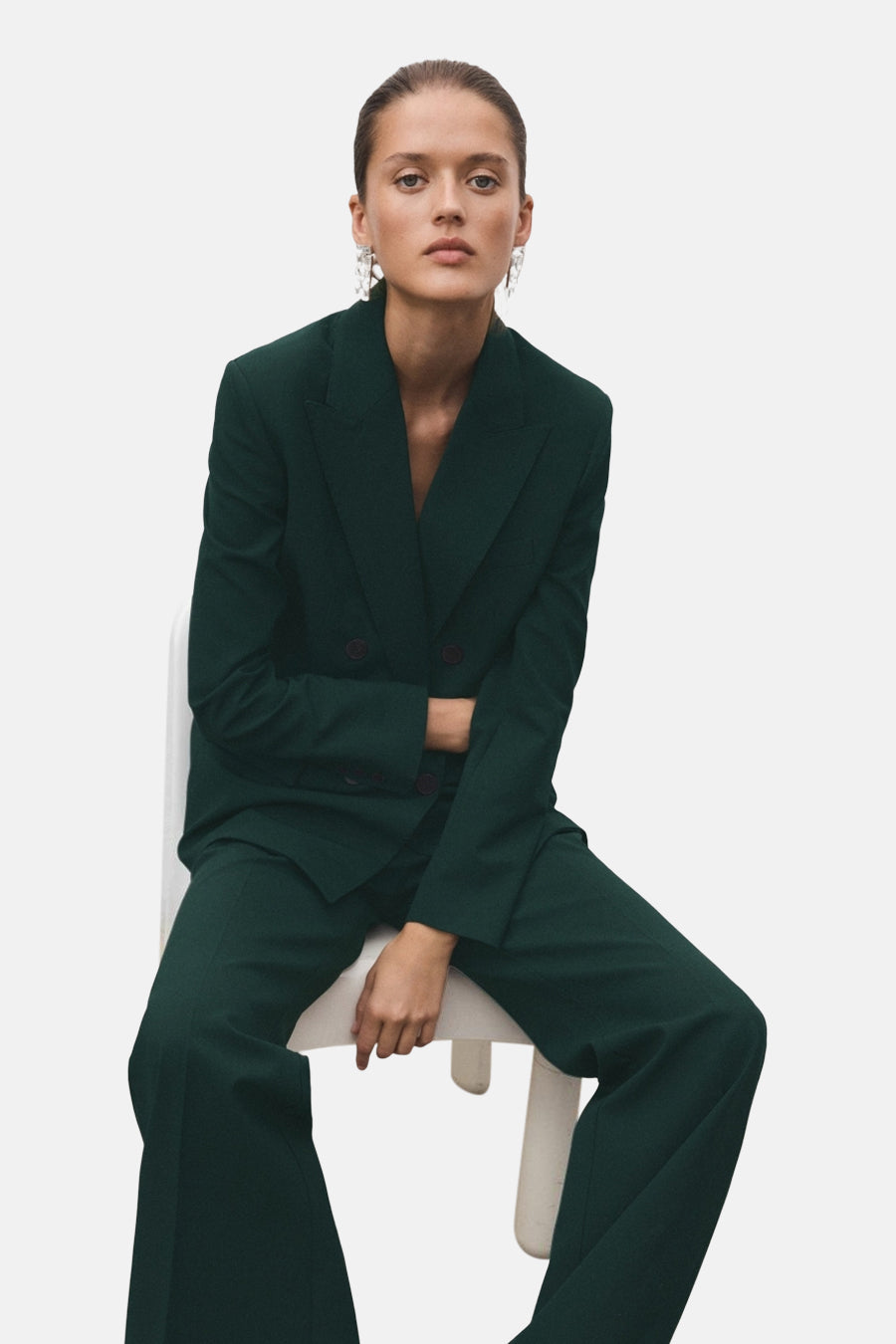 Groene blazer van MANGO, gedragen door een zittende vrouw met lange oorbellen.
