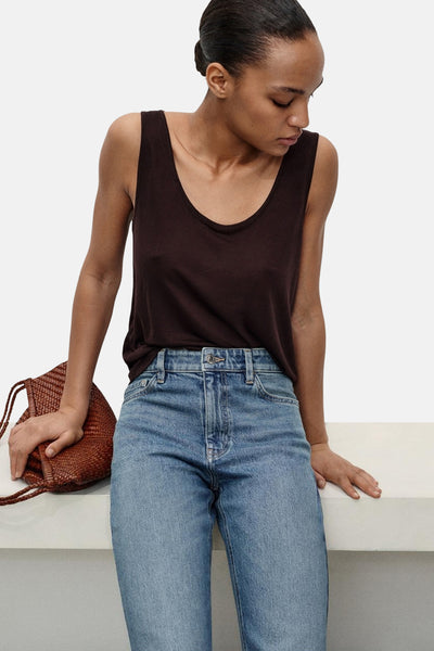 Jean Mom bleu moyen de MANGO, porté avec un débardeur marron et un sac tressé en cuir.