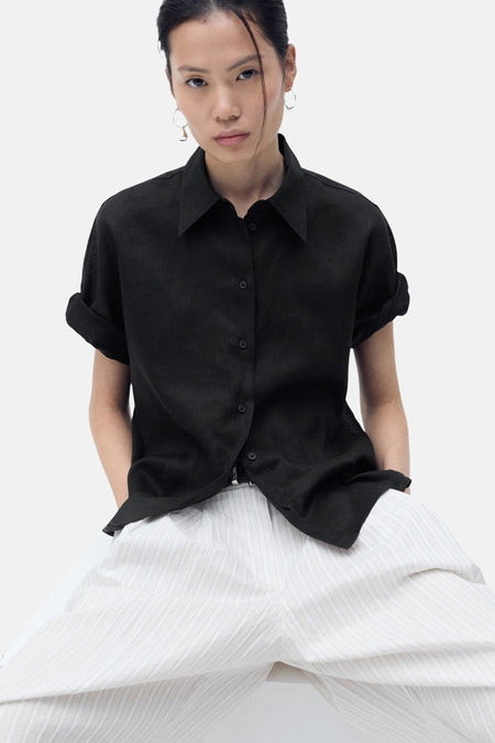 Zwarte blouse met korte mouwen van MANGO, gedragen met een gestreepte broek en oorbellen.