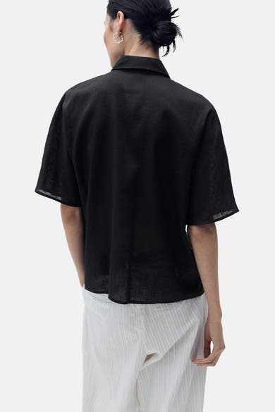 Zwart overhemd met korte mouwen van MANGO, van achteren gezien, gedragen met een gestreepte broek.