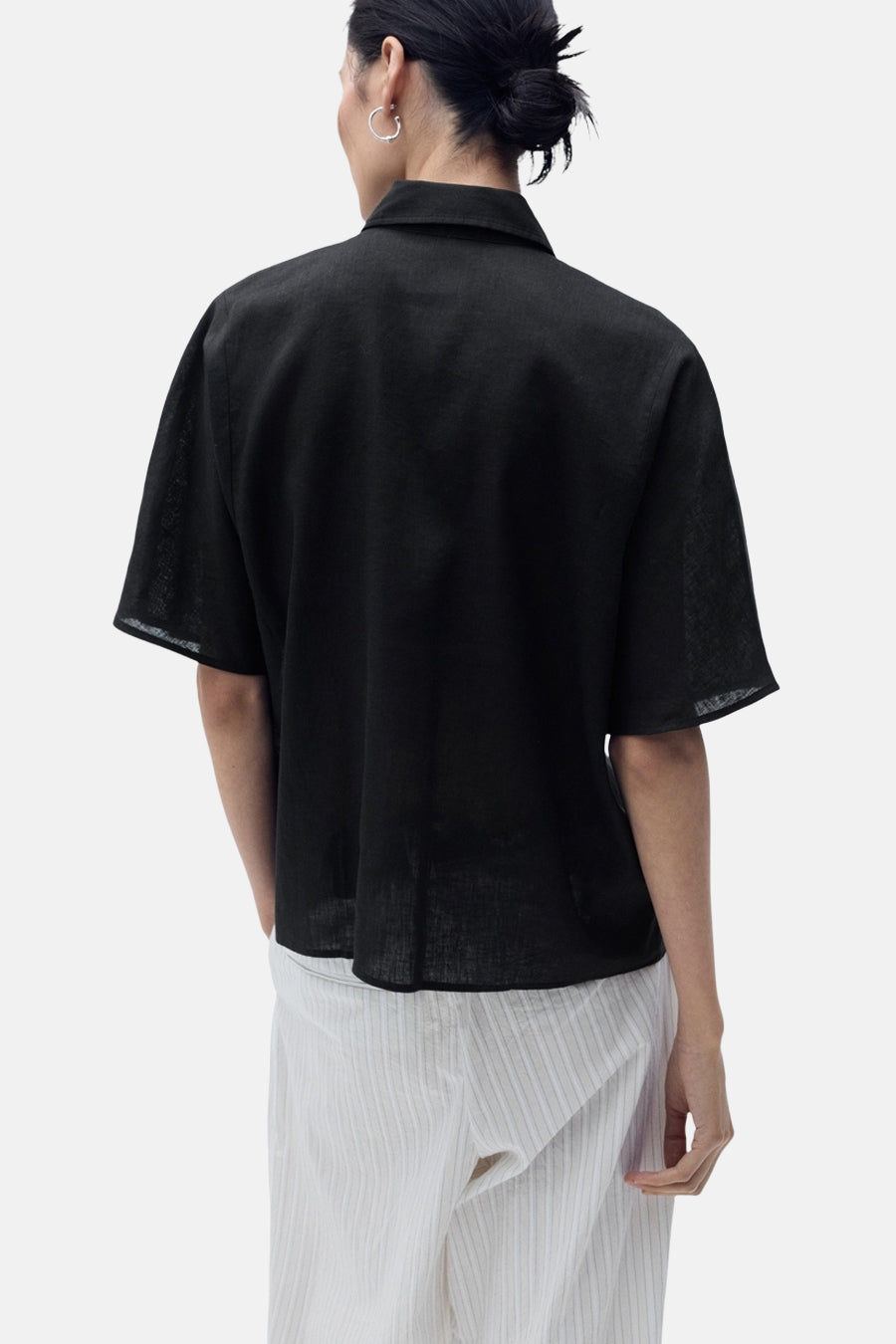 Zwart overhemd met korte mouwen van MANGO, van achteren gezien, gedragen met een gestreepte broek.
