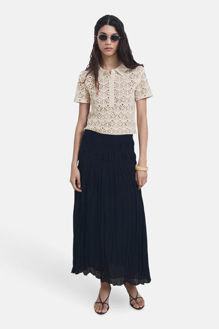 Beige ronde hals trui van MANGO, met een gehaakte textuur, gedragen met een lange zwarte rok en sandalen.