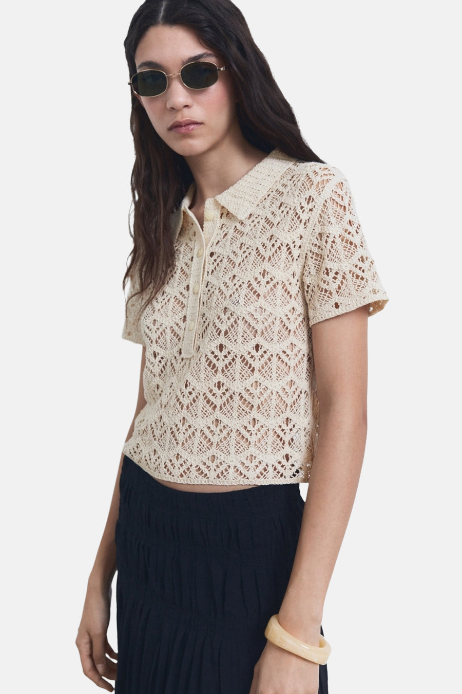 Beige ronde hals trui van MANGO, met ajourpatroon, gedragen met een donkere rok en een zonnebril.