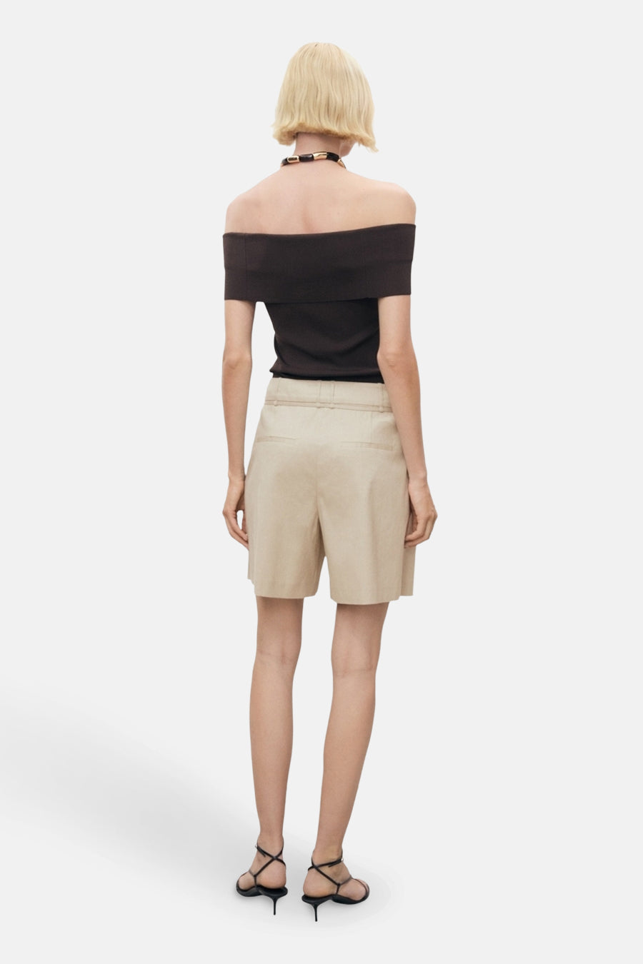 Beige Bermuda van MANGO, met zijzakken en een hoge taille, gedragen met een zwarte top en sandalen met hak.