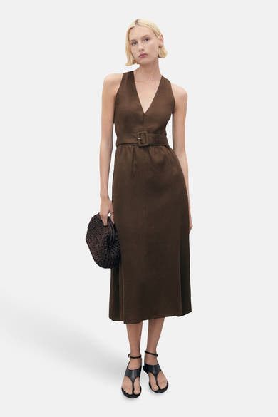 Robe marron ceinturée par MANGO, coupe midi, avec encolure en V et une personne portant des sandales et tenant un sac à main.
