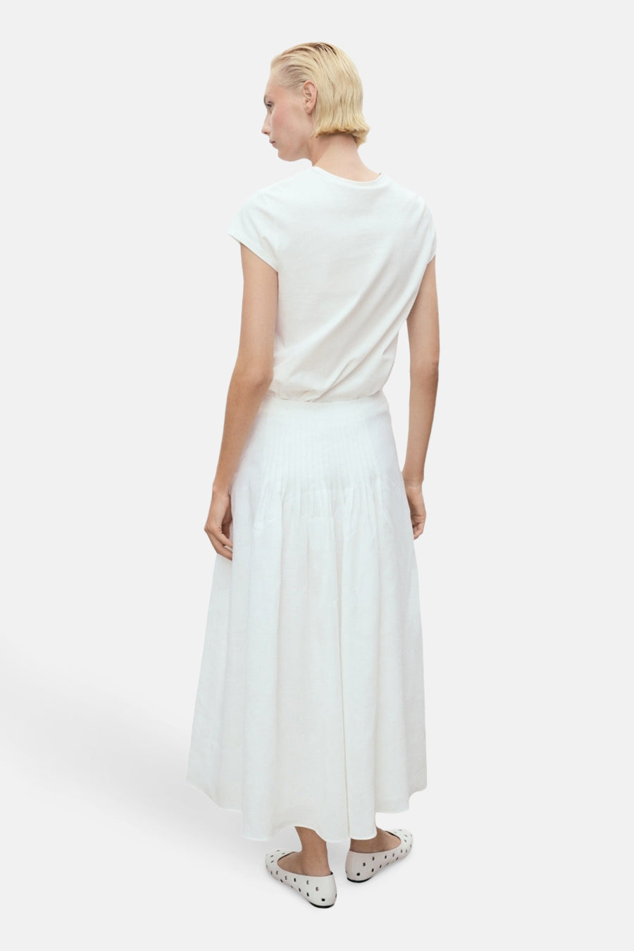 Wit T-shirt met korte mouwen van MANGO, gedragen met een witte plooirok en stippenballerina's.