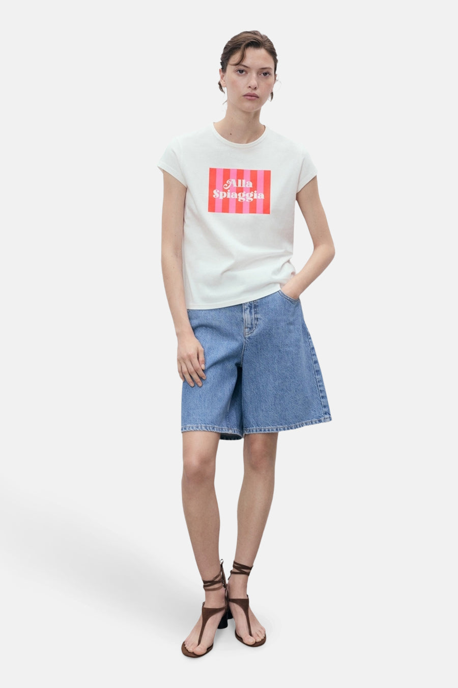 Wit T-shirt met korte mouwen van MANGO, met kleurrijk grafisch patroon, gedragen met een blauwe spijkerbroek met korte pijpen en sandalen met hak.