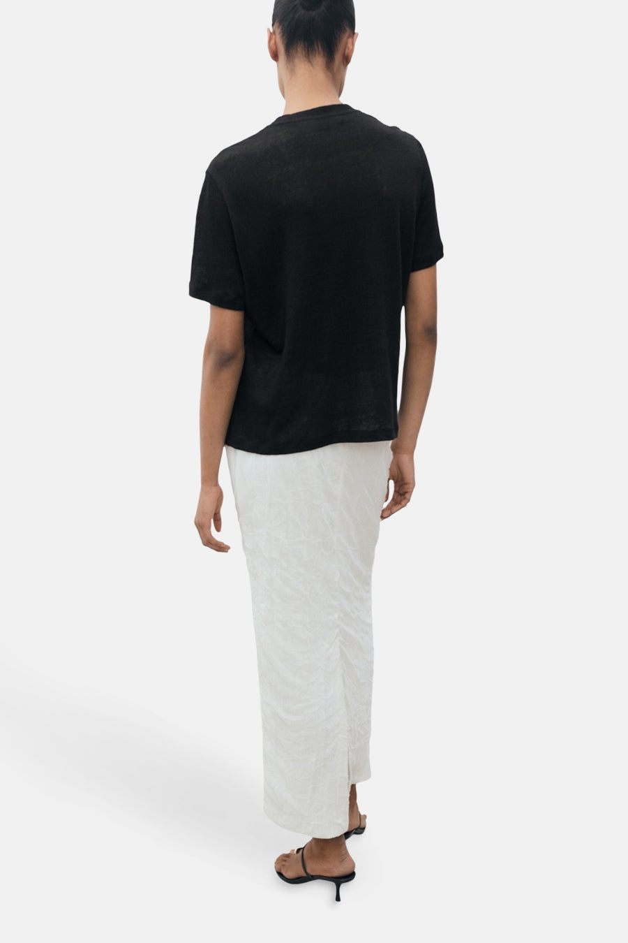 Zwart T-shirt met korte mouwen van MANGO, gedragen met een lange witte textuurrok en zwarte sandalen met hak.