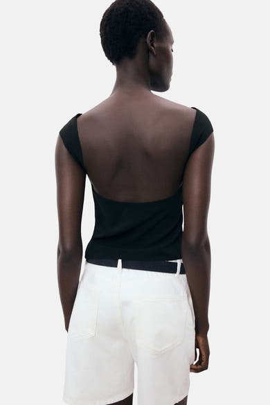 Zwart T-shirt met korte mouwen van MANGO, gedragen met een witte short met hoge taille en zwarte riem.