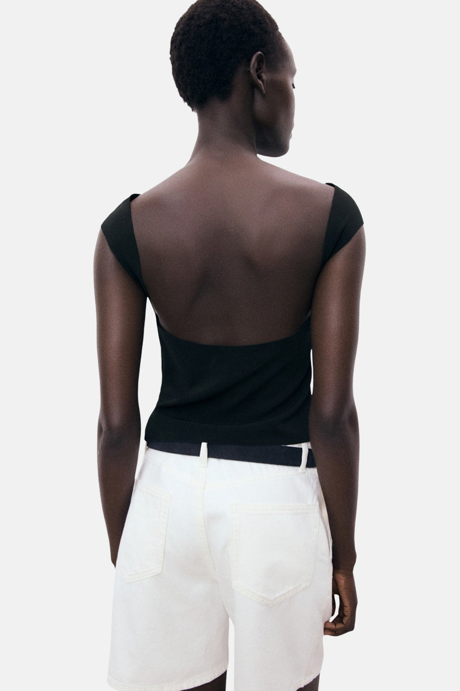 Zwart T-shirt met korte mouwen van MANGO, gedragen met een witte short met hoge taille en zwarte riem.