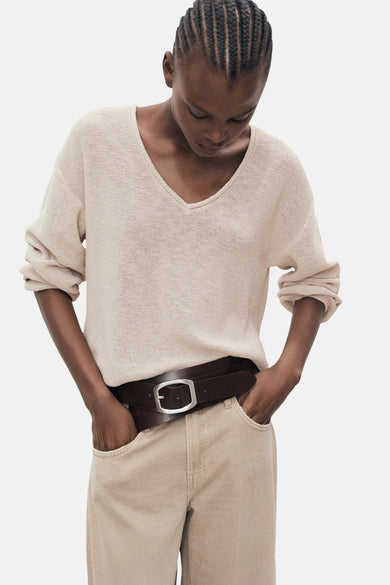 Pull à col en V beige de MANGO, porté avec un pantalon beige et une ceinture en cuir marron.