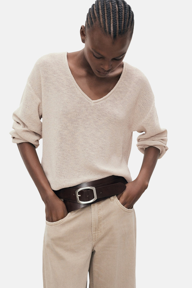Pull à col en V beige de MANGO, porté avec un pantalon beige et une ceinture en cuir marron.