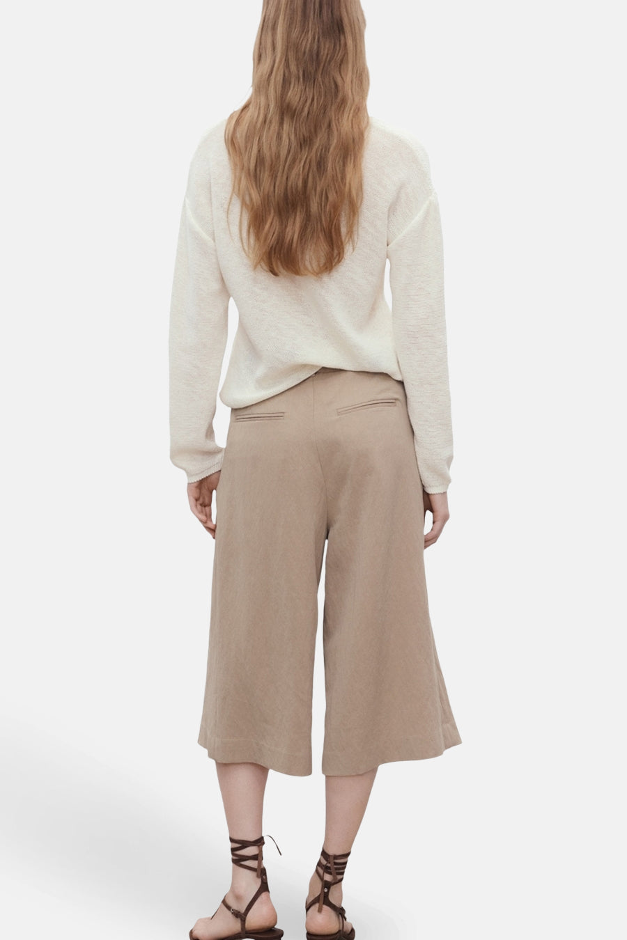 Pull à col en V blanc de MANGO, porté avec un pantalon culotte beige et des sandales à lanières.