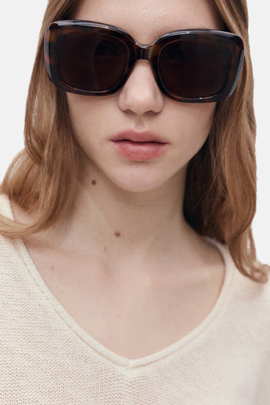 Pull à col en V blanc de MANGO, en maille fine portée avec des lunettes de soleil.
