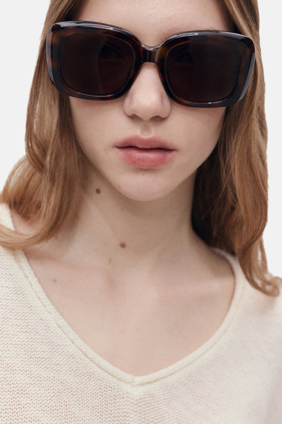 Pull à col en V blanc de MANGO, en maille fine portée avec des lunettes de soleil.
