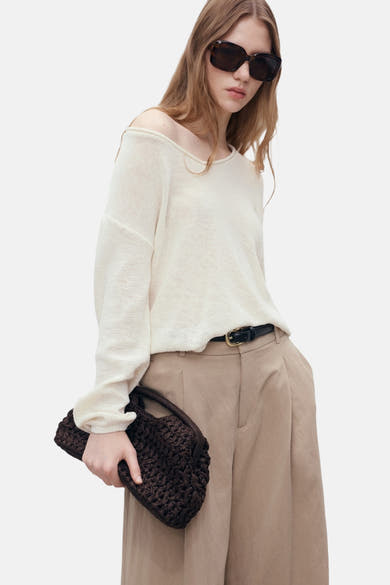 Pull col en V blanc de MANGO, porté avec un pantalon beige et une ceinture noire.