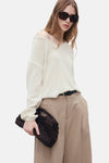 Pull col en V blanc de MANGO, porté avec un pantalon beige et une ceinture noire.