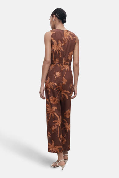 Bruin pak met palmboomprint van MANGO, van achteren gezien met witte sandalen met hak.