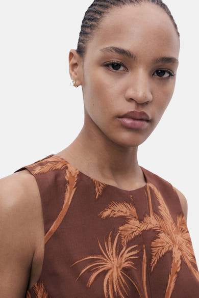 Bruin MANGO-pak met oranje palmboomprint, gedragen met kleine gouden oorbellen.