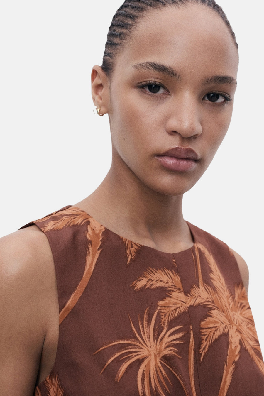 Bruin MANGO-pak met oranje palmboomprint, gedragen met kleine gouden oorbellen.