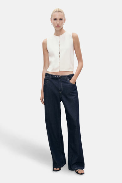 Gilet blanc de MANGO, boutonné, porté avec un jean taille basse bleu foncé à ceinture.