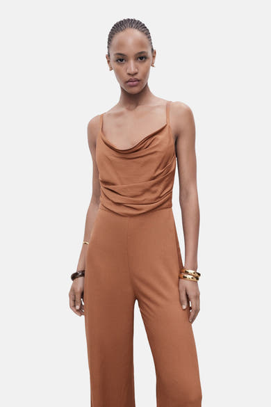Bruin jumpsuit van MANGO, losse pasvorm, met gedrapeerde halslijn en gouden sieraden.