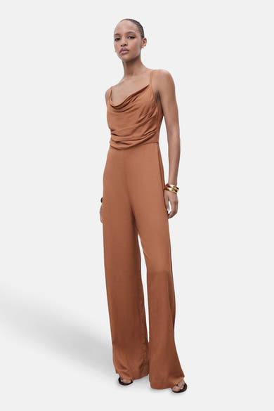 Bruin jumpsuit van MANGO, losse pasvorm met gedrapeerde halslijn en gouden armbanden.