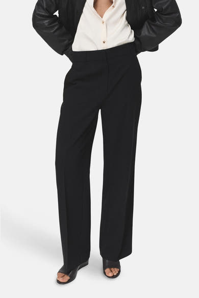 Pantalon noir de MANGO, coupe droite et jambes larges, porté avec une chemise et une veste noires.