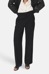 Pantalon noir de MANGO, coupe droite et jambes larges, porté avec une chemise et une veste noires.