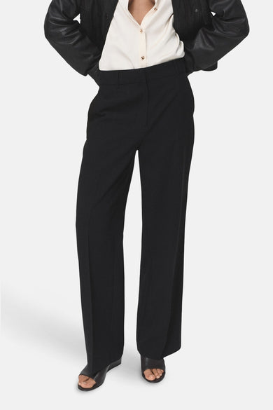 Pantalon noir de MANGO, coupe droite et jambes larges, porté avec une chemise et une veste noires.