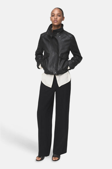 Pantalon noir de MANGO, coupe ample, porté avec une chemise crème et une veste en cuir noir.