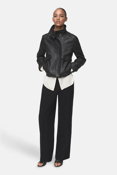 Pantalon noir de MANGO, coupe ample, porté avec une chemise crème et une veste en cuir noir.